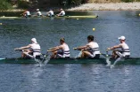 Im Vordergrund befinden sich die 4 Ruderer der RUB während des Rennens in ihrem Boot, im Hintergrund ist ein Boot der Konkurrenz mit vier anderen Sportlern.