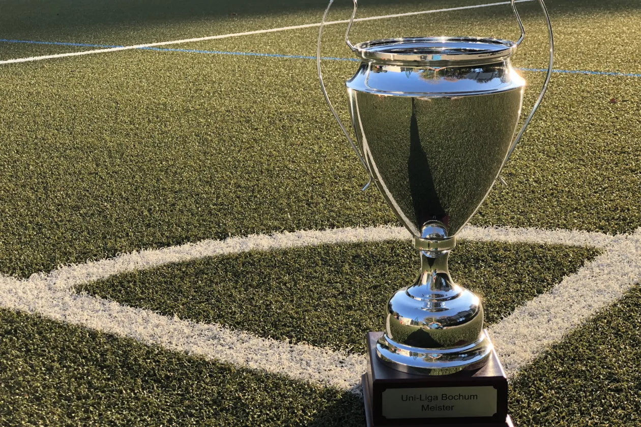Ein silberner Pokal in der Ecke stehend auf einem Kunstrasenplatz.