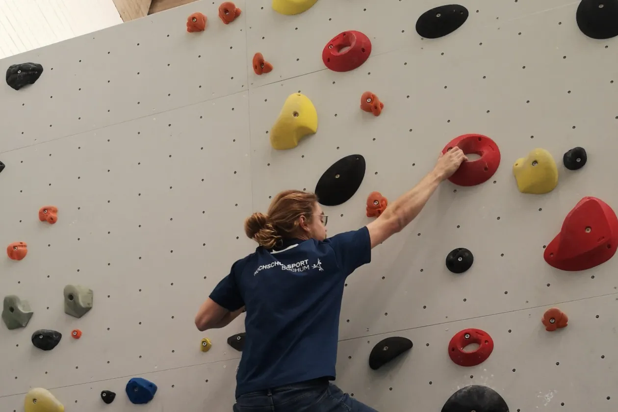 Eine Person klettert an einer Kletterwand mit bunten Steinen hoch