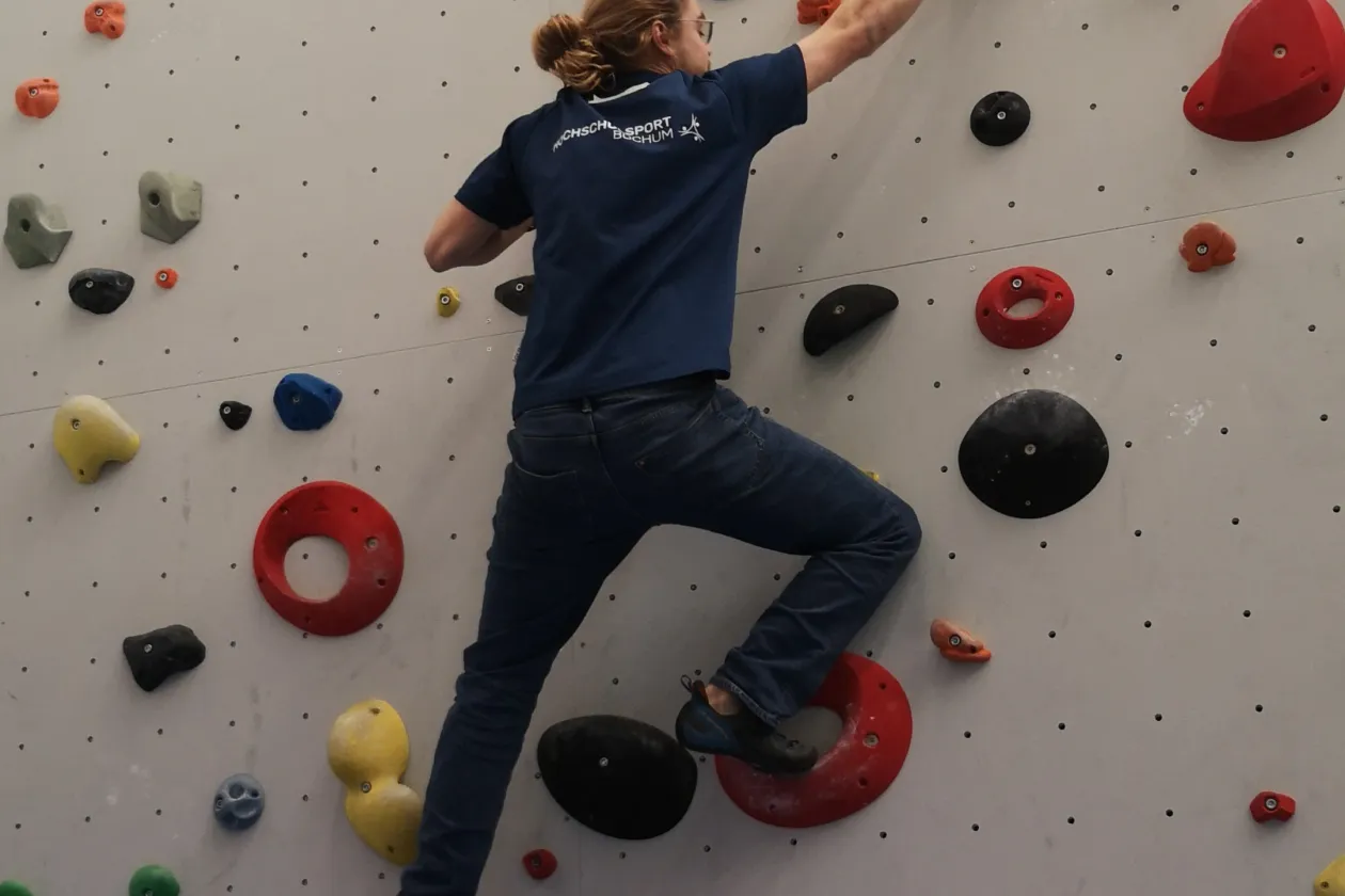 Eine Person klettert an einer Kletterwand mit bunten Steinen hoch
