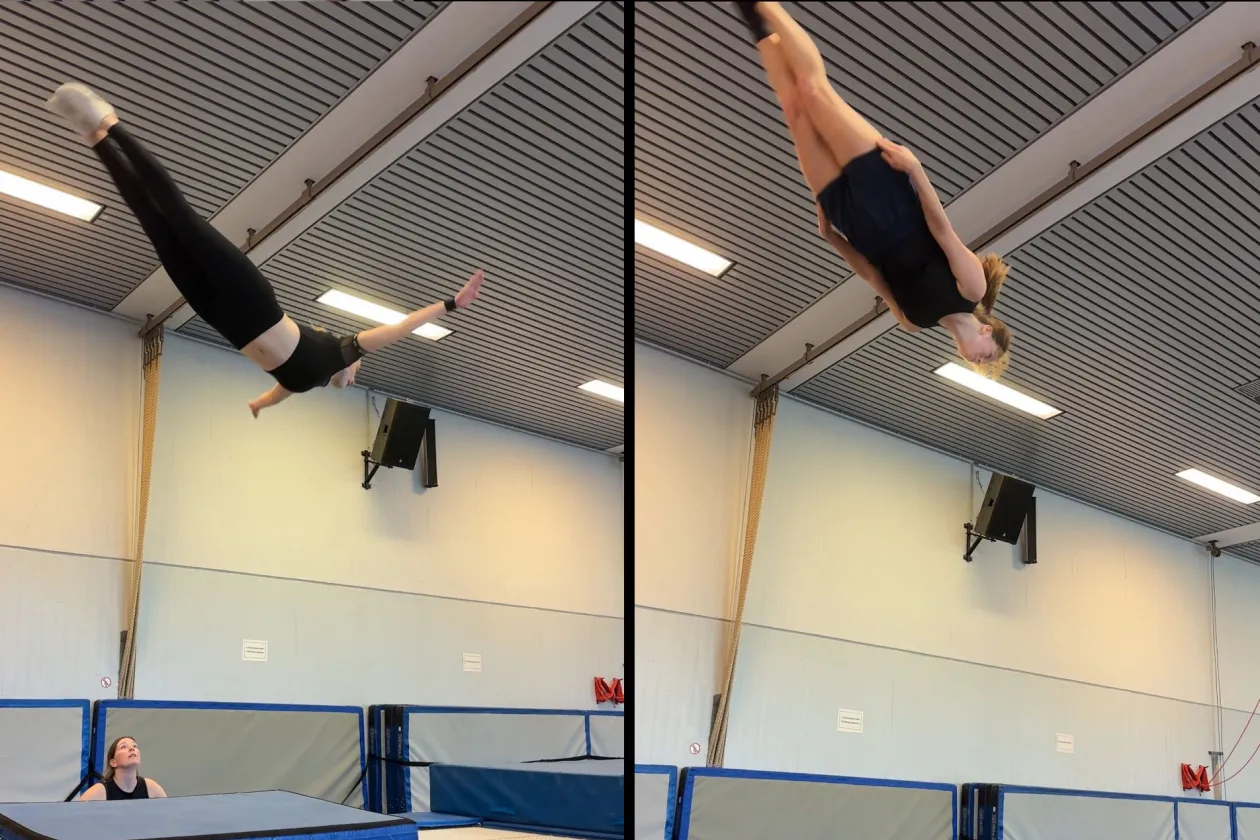 bildbeschreibung 1-2 sätze  Eine Person führt in einer Turnhalle einen Sprung auf einem Trampolin aus und ist hoch in der Luft zu sehen. Unter ihr stehen Sicherheitsmatten, während eine andere Person vom Rand aus nach oben schaut.