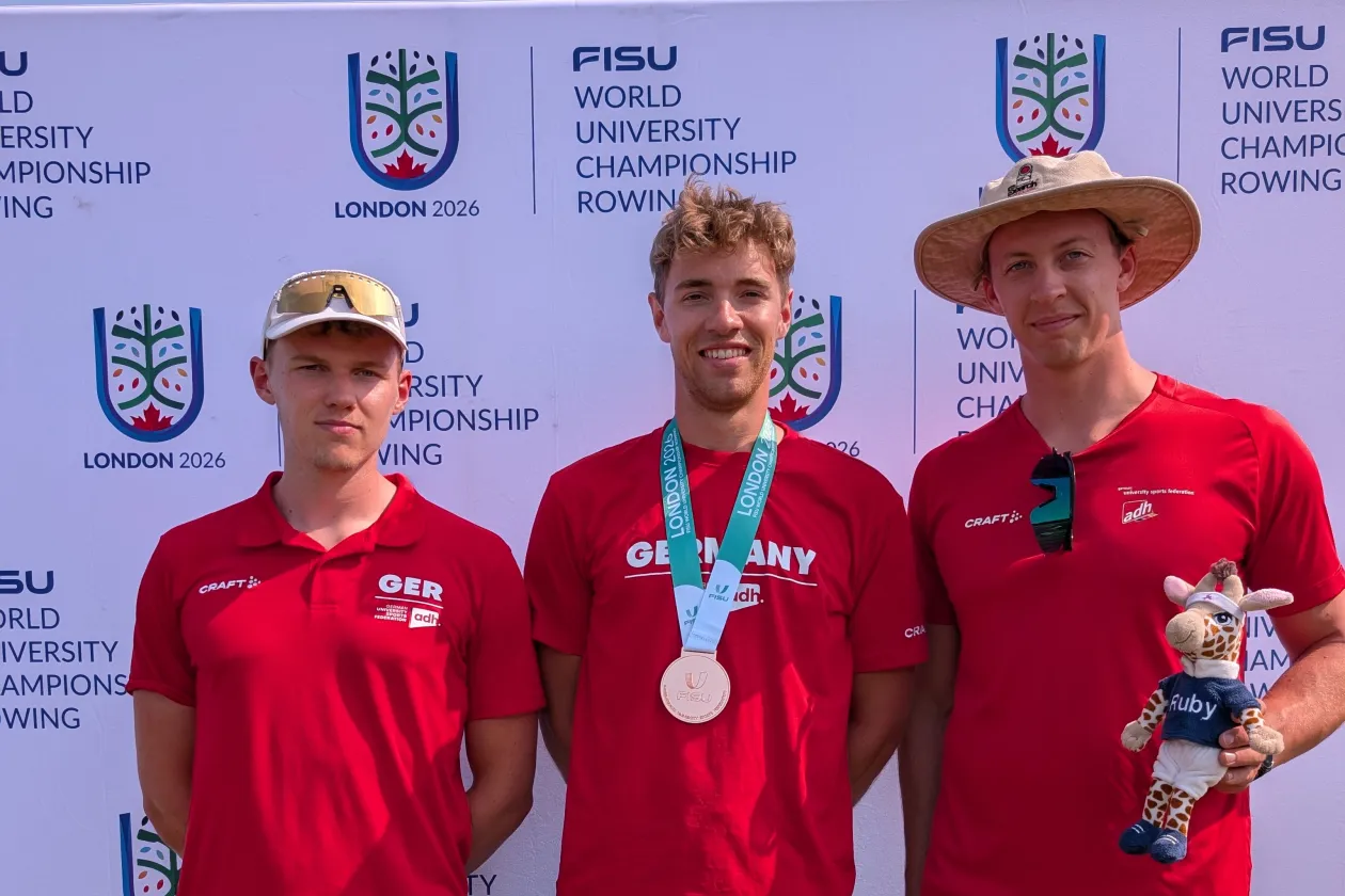 Die 3 Ruderer Sven Achterfeld, Kaspar Virnekäs und Tom Tewes posieren zum Foto. Kaspar trägt seine Bronzemedaille und Tom hält das Maskottchen vom Hochschulsport.