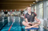 Der Spitzensportler Poul Zellmann sitzt im Schwimmbad auf einem Startblock und blättert dabei in einem Buch.