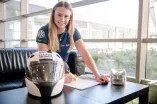 Spitzensportlerin Laura Nolte unterschreibt ein Dokument. Neben Ihr steht ein Bobhelm auf dem Tisch.