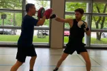 Zwei Personen stehen sich gegen&uuml;ber. Eine Person boxt mit Boxhandschuhen in die Handpratze der anderen Person.