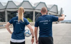 Mitsrbeiterin und Mitarbeiter des Hochschulsports mit Sportgeräten vor dem Audimax.
