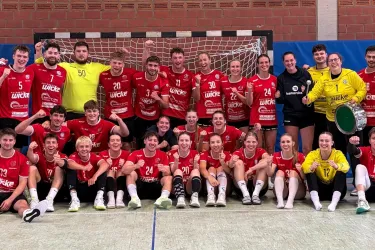 Die Handballherren und -damen der RUB stehen und sitzen in und um ein Handballtor zusammen mit ihren Trainern.