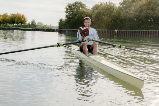 Der Spitzensportler Felix Wimberger sitzt in einerm Ruderboot auf dem Kanal und liest dabei ein Buch.