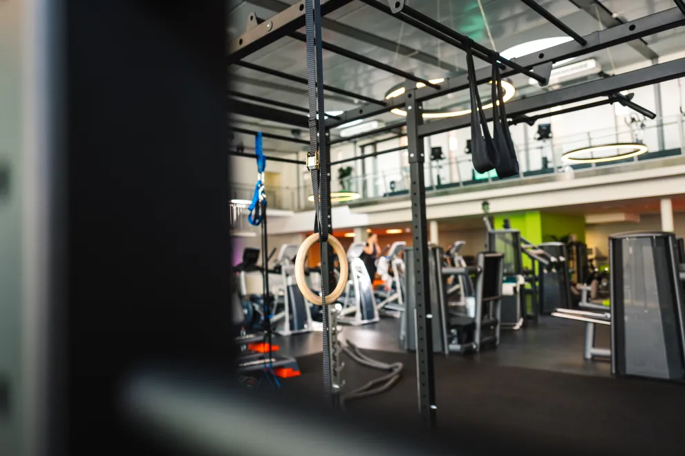 Modern fitness area featuring a functional training rig, gymnastic rings, and strength equipment in a bright, open gym environment.