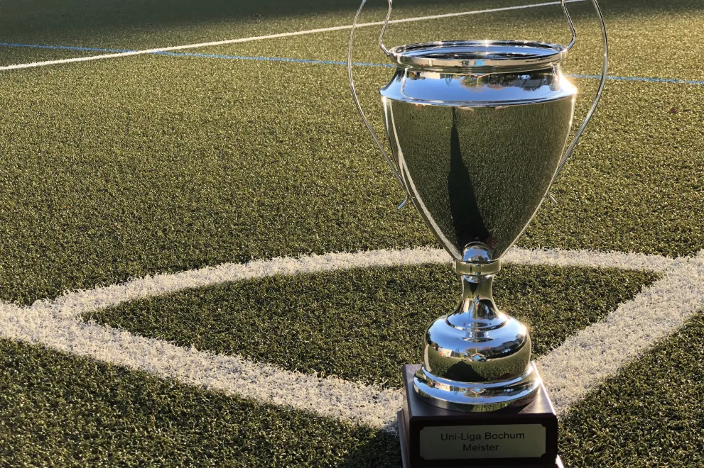Ein silberner Pokal in der Ecke stehend auf einem Kunstrasenplatz.
