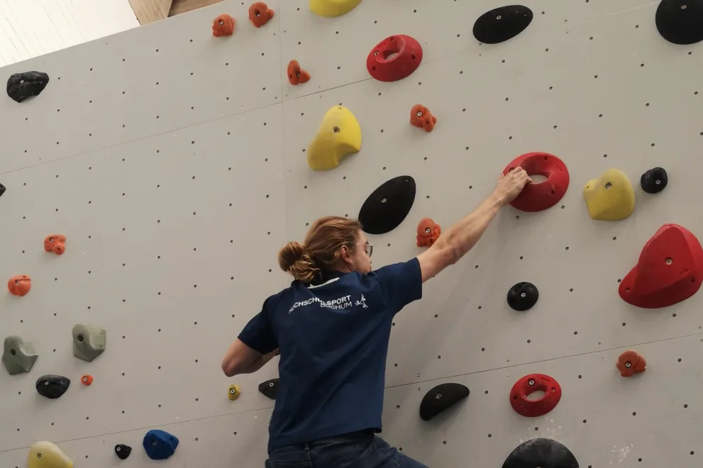 Eine Person klettert an einer Kletterwand mit bunten Steinen hoch