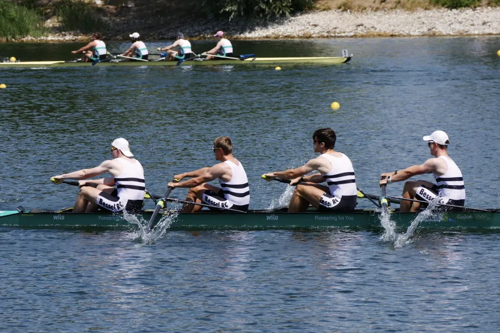 Im Vordergrund befinden sich die 4 Ruderer der RUB während des Rennens in ihrem Boot, im Hintergrund ist ein Boot der Konkurrenz mit vier anderen Sportlern.