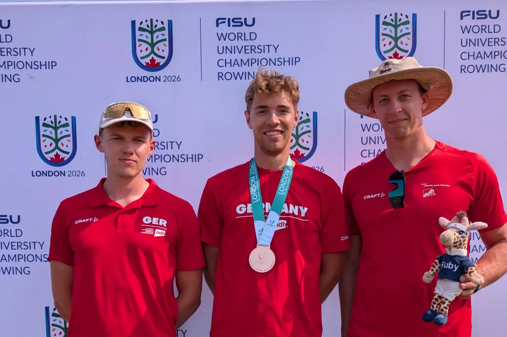 Die 3 Ruderer Sven Achterfeld, Kaspar Virnekäs und Tom Tewes posieren zum Foto. Kaspar trägt seine Bronzemedaille und Tom hält das Maskottchen vom Hochschulsport.